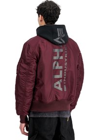 Bordeauxfarbige Bomberjacke mit gerippten Bündchen und Saum, mit einem grauen Logo auf dem Rücken und einer schwarzen Kapuze, die herausragt. Glatte Textur, gepolstertes Design.