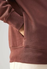 Barna pamut pulóver laza szabásban, látható varrási részletekkel, bordás mandzsettákkal és elülső oldalzsebbel.