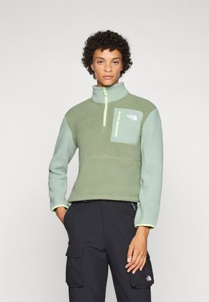 Grønn fleece-pullover med halv-zip krage, glidelås lomme på brystet og kontrasterende gule detaljer på glidelåsen og mansjettene.