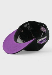 Musta baseball-lippalakki, jossa on violetti lippa. Sivussa brodeerattu logo ja sisätagit. Pehmeää kangasta, jossa on ommeltuja yksityiskohtia.