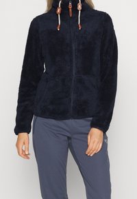 Veste en polaire bleu marine avec fermeture éclair à l'avant, col haut et cordons de serrage ajustables ; dispose de deux poches avant et d'un tissu texturé.