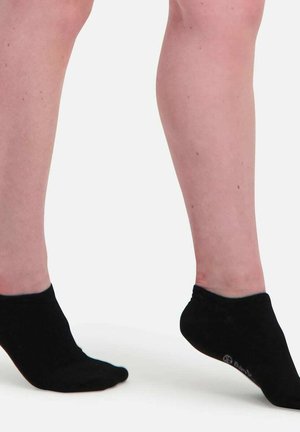 Lower legs and feet wearing black ankle socks, one foot flat on ground and the other slightly raised on toes against a plain background.