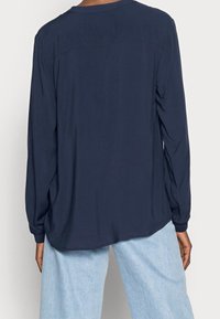 Navy long-sleeve shirt with a relaxed fit, smooth texture, round neckline, and slightly dropped shoulders, paired with light blue pants.