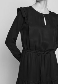 Schwarzes langärmliges Kleid mit gerafften Schultern, Schlüsselloch-Ausschnitt und Kordelzug in der Taille. Weiche Textur und gestuftes Rockdesign.