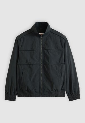 Jachetă neagră ușoară cu fermoar, guler drept, mâneci lungi, manșete și tiv elastice și două buzunare frontale.