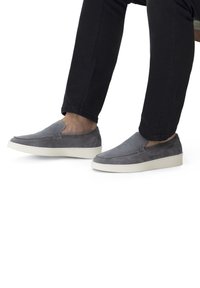 Graue Wildleder-Slipper mit einer weißen Gummisohle, die eine glatte Textur und eine gestickte Detailverarbeitung entlang der Kanten aufweisen.
