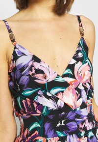 Robe fleurie avec un fond noir orné de fleurs violettes et roses. Bretelles spaghetti avec anneaux dorés, décolleté en V profond.