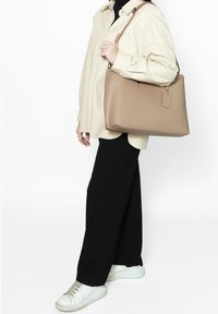 Beige leren tote bag met een gestructureerde vorm, korte handvaten en een label detail. Gecombineerd met een licht shirt en zwarte wijde broek.