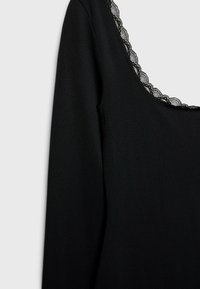 Schwarzes Langarmoberteil mit weitem Ausschnitt, verziert mit zarter schwarzer Spitzenborte am Rand. Glattes Material mit figurbetontem Schnitt.