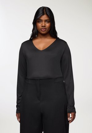 Maglietta nera a maniche lunghe con scollatura a V, realizzata in materiale liscio, abbinata a pantaloni neri a vita alta con tasche laterali.