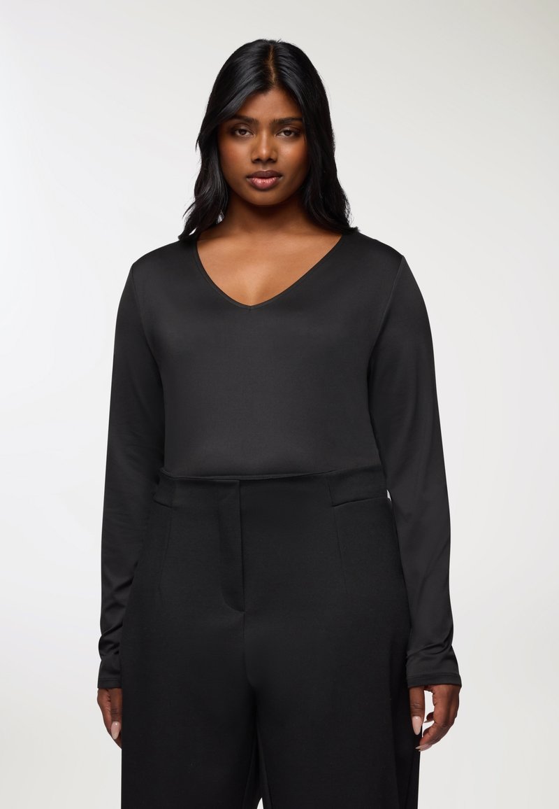 Czarna bluzka z długim rękawem i dekoltem w serek, wykonana z gładkiego materiału, zestawiona z czarnymi spodniami typu high-waisted z bocznymi kieszeniami.