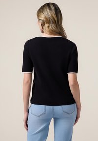 Top scurt negru cu mâneci scurte și guler rotund, având gambă albă pe mâneci și tiv. Modelul poartă blugi de culoare albastră deschisă.