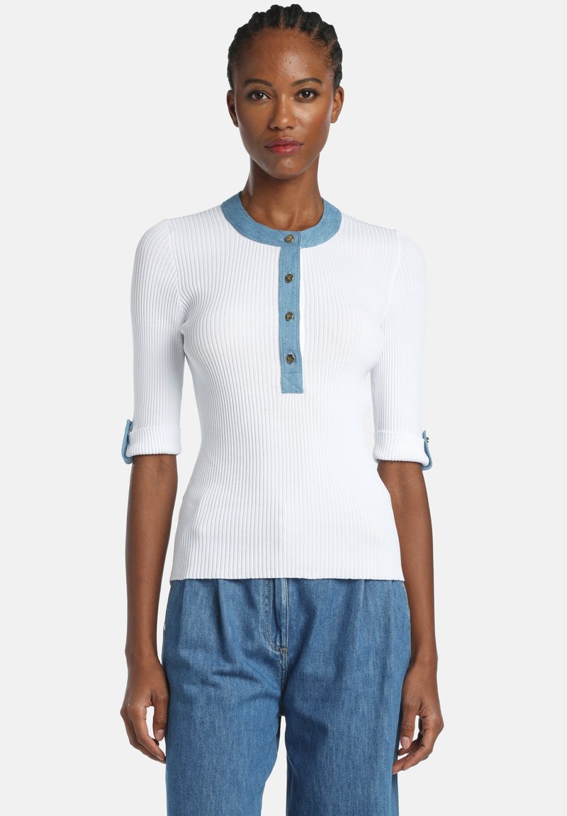 Haut blanc côtelé avec un col en denim, quatre boutons à l'avant, et des manches retroussées avec des détails boutons. Associé à un pantalon en denim bleu.