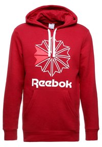 Sudadera roja con bolsillo canguro, cordones blancos y un gran gráfico de un diseño de estrella geométrica. Presenta el logo de "Reebok" en blanco.
