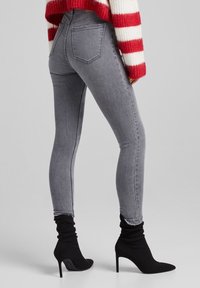 Šedé skinny džíny s hladkou texturou a designem pěti kapes, spárované s černými kotníkovými botami s špičatou špičkou a vysokým podpatkem.