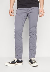 Grijze slim-fit chino's met een gladde textuur, voorzakken en subtiele stiksels, gecombineerd met zwarte canvas sneakers.