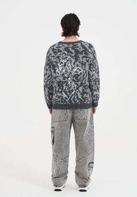 Grijze, fuzzy trui met een gedurfde witte grafische ontwerp op de rug; gecombineerd met losse, grijze, gemêleerde cargobroek met zakken.