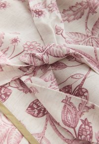 Tissu crème avec une texture froissée présentant des motifs floraux et de feuilles mauves ainsi qu'une fine bande dorée le long d'un bord.