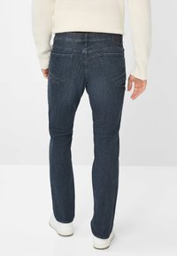 Jeans in denim blu scuro con taglio dritto, dotati di tasche posteriori e di un'etichetta in pelle sulla vita, abbinati a sneakers bianche.