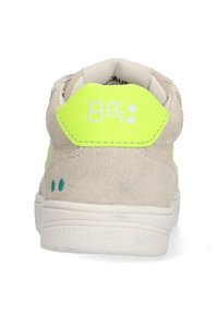 Beige suede sneaker with a bright yellow heel tab, featuring white branding and small aqua accents near the sole. Low-top design.