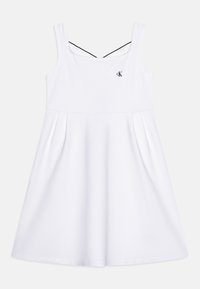 Vestido blanco sin mangas con un cuerpo ajustado y una falda acampanada, que presenta un diseño de tirantes cruzados y un pequeño logo en el pecho.