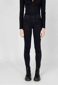 Jeans neri skinny con vita intermedia, realizzati in denim. Indossati con stivali neri con lacci, caratterizzati da una texture liscia e senza decorazioni visibili.