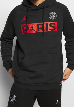Sweat à capuche noir avec texte rouge "PARIS" et logo Jumpman, associé à un pantalon noir avec les logos Paris Saint-Germain et Jumpman.