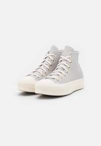 Hoge sneakers van lichtgrijs leer met witte veters, gouden oogjes en een getextureerde crèmekleurige rubberen zool met een ronde neus.