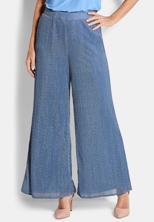 Blaue, breitbeinige, strukturierte Hose, getragen von einer stehenden Person mit einer Hand in der Hüfte, kombiniert mit hautfarbenen High-Heels.