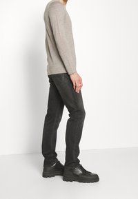 Hellgraues Langarmshirt, schwarze Slim-Fit-Jeans und schwarze Schuhe mit dicker Sohle, Seitenansicht mit glatter Textur und gerader Silhouette.
