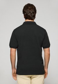 Svart pikétröja med krage och korta ärmar, tillverkad av ett strukturerat tyg. Designad för en standardpassform med rak fåll.