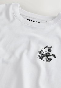 T-shirt blanc à col rond avec un petit chat noir en style croquis marchant sur la zone de la poitrine.