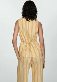 Striped, sleeveless yellow top with a tied waist. The fabric appears lightweight and textured, complemented by matching wide-leg trousers.