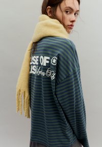 Vihreä- ja laivastonsinisin raidallinen pitkähihainen paita, jossa valkoiset graafiset tekstit ja rento istuvuus, yhdistetty keltaiseen, teksturoituun huiviin, jossa on hapsutetut reunat.