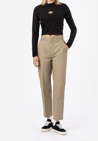 Svart långärmad croppad skjorta med en liten logotyp på bröstet, kombinerad med ljusbeige högmidjade byxor och svarta sneakers.