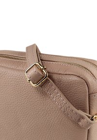 Kompakte Ledertasche in weichem Beige mit einer strukturierten Oberfläche, goldfarbenen Beschlägen und einem Reißverschluss mit funktionalem Riemen.