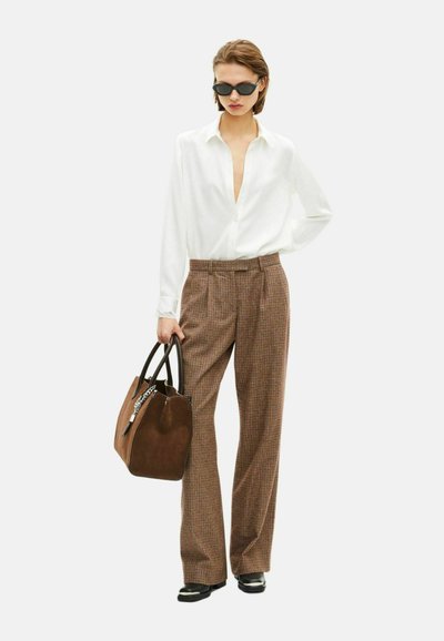 Hvid skjorte med knapper, ternede brune bukser, sorte solbriller, bærer en brun suedes håndtaske med kæde detalje og sorte håndtag.