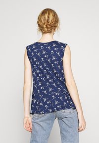 Navy blue sleeveless top with white floral pattern, soft fabric, relaxed fit, rounded neckline, and side slits. Worn with light blue jeans.