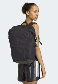 Zaino nero con spallacci imbottiti, molteplici scomparti con zip e una finitura testurizzata. Presenta un logo discreto sulla parte anteriore e tasche laterali.