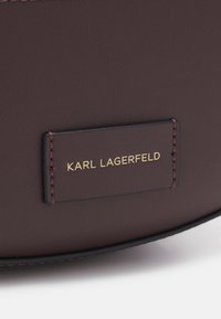 Surface en cuir marron avec une étiquette rectangulaire cousue, embossée du texte "KARL LAGERFELD" en lettres dorées.