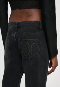 Black denim jeans with a high waist, featuring a distinct embossed "C" design on the back pocket and a smooth textured finish.