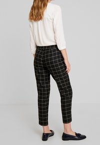 Czarno-białe spodenki w kratę o dopasowanym kroju, ze mankietami u dołu i gładką teksturą, zestawione z jasną bluzką i granatowymi mokasynami.