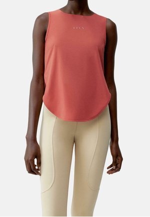 Korasowy top bez rękawów z zaokrąglonym dołem noszony przez osobę o ciemnej karnacji, w połączeniu z beżowymi legginsami z wysokim stanem i detalami szwów.