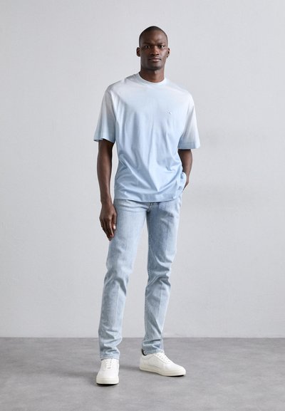 Ανοιχτού μπλε gradient μπλουζάκι κοντό μανίκι, συνδυασμένο με ανοιχτού μπλε τζιν και λευκά αθλητικά παπούτσια. Απλό σχέδιο, λεία υφή.