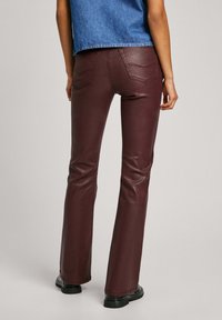 Burgundy flared jeans made of a smooth, glossy material. Features five pockets with curved stitching details. Worn with a denim top.