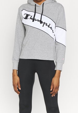Grauer Hoodie mit schwarzen Akzenten und weißem, gestreiftem Text, auf dem in geschwungener Schrift das Wort "Champion" über die Brust steht. Lange Ärmel, Baumwollmischung.