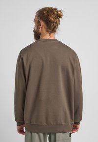 Felpa marrone con collo a giro, maniche lunghe, polsini e orlo a costine. Il tessuto sembra morbido con una consistenza liscia. Design semplice e uniforme.