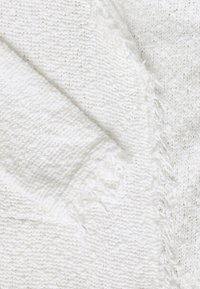 Biały tkanina tkana o teksturowanym, miękkim wykończeniu. Charakteryzuje się postrzępionymi krawędziami i delikatnym połyskiem, co tworzy przytulny wygl�ąd.