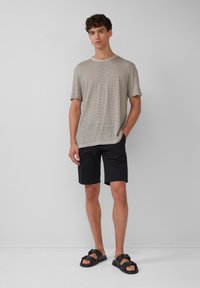 Gestreiftes T-Shirt in Tan und Creme, schwarze Shorts und schwarze Sandalen. Lässiger Schnitt mit kurzen Ärmeln, Rundhalsausschnitt und Shorts in Oberschenkellänge.
