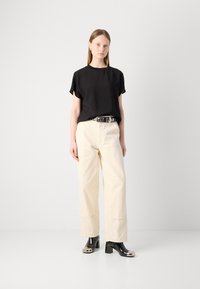Haut noir à manches courtes, pantalon crème à jambes larges et bottes à talons noires brillantes avec accents argentés aux orteils. Style simple et décontracté ; textures lisses.